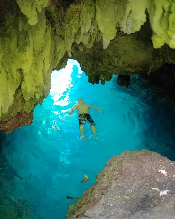 Swimmer in the turquoise pool of Halo Tabung cave under hanging rock