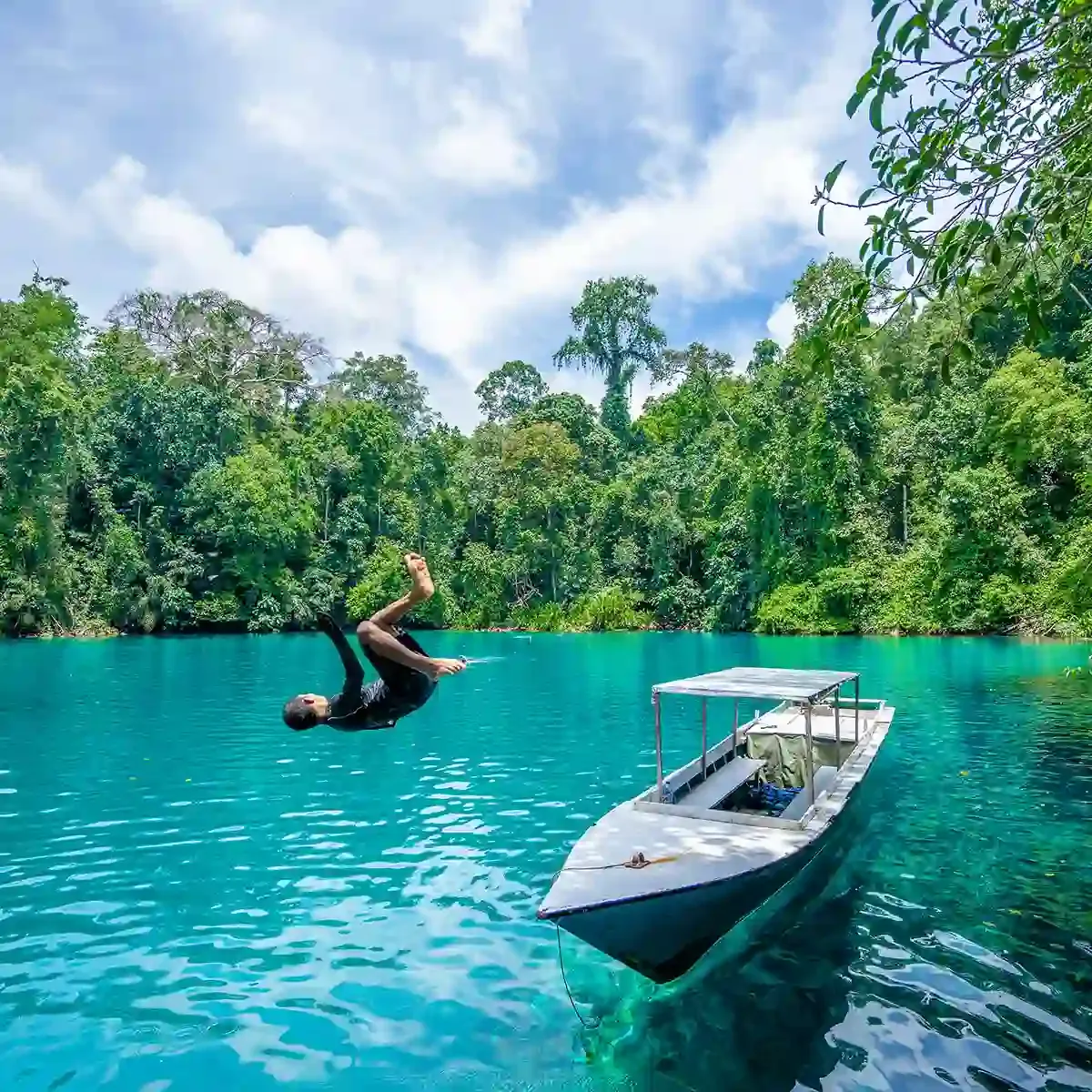 Swimmer back-flipping off a boat into the clear water of Labuan Cermin