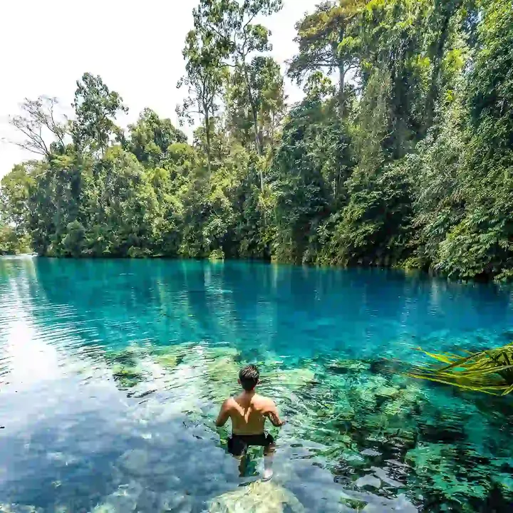 Man wading into clear water below jungle at Labuan Cermin