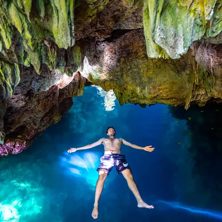 Swimmer floating in a blue cave pool under stalactites on Maratua